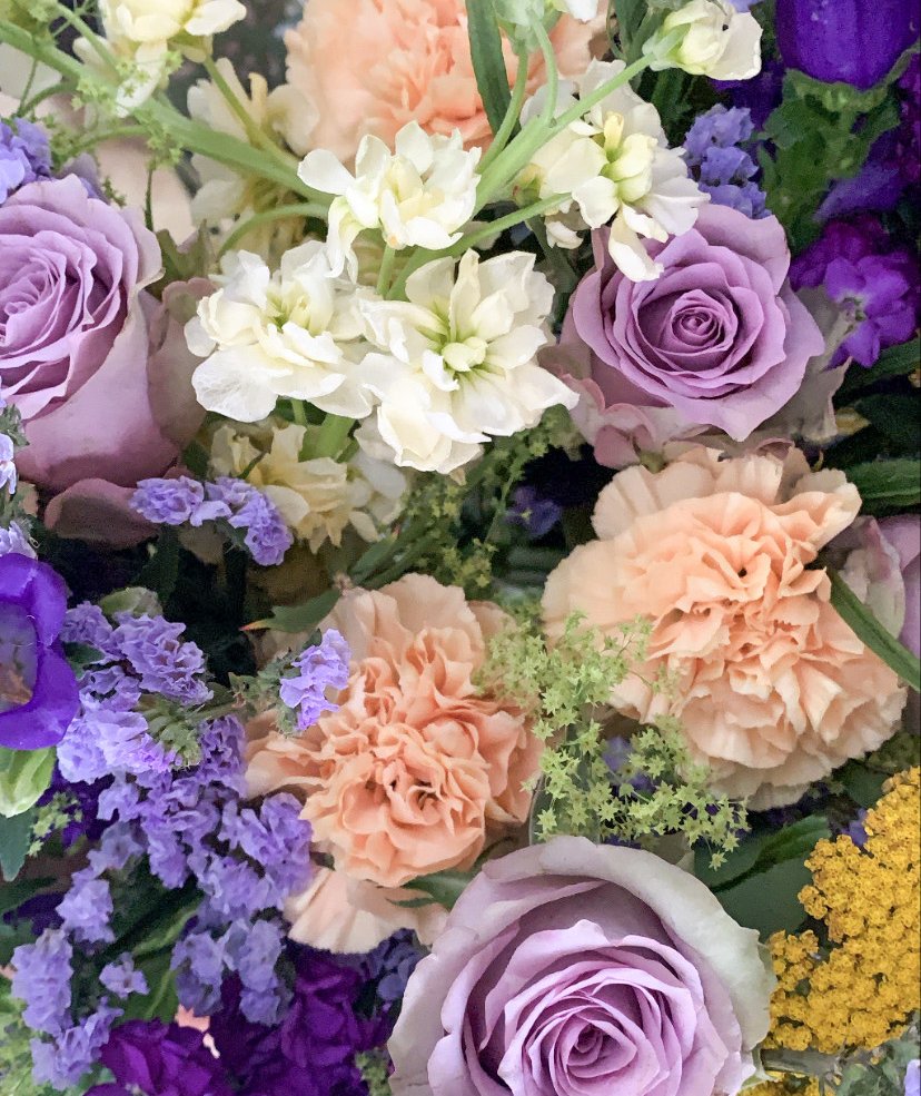 A bouquet of lilac roses, peach carnations, white and purple stocks, statice and yellow achillea