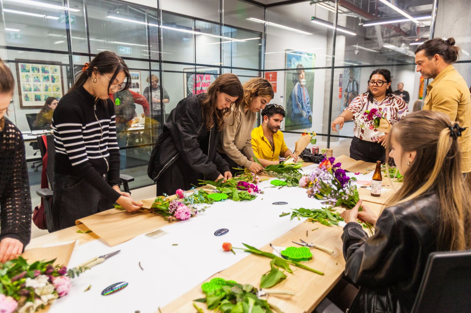 Farah guiding a group as they build bouquets around a long table covered in stems and kraft paper